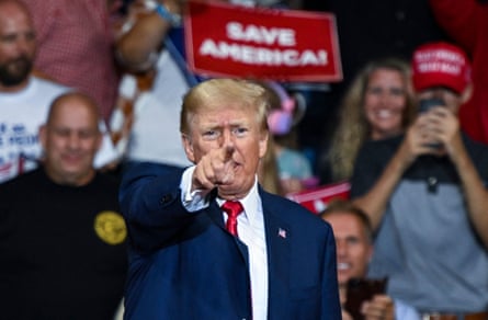 Donald Trump points a finger out to the camera as supporters behind him hold 'Save America!'  signs.